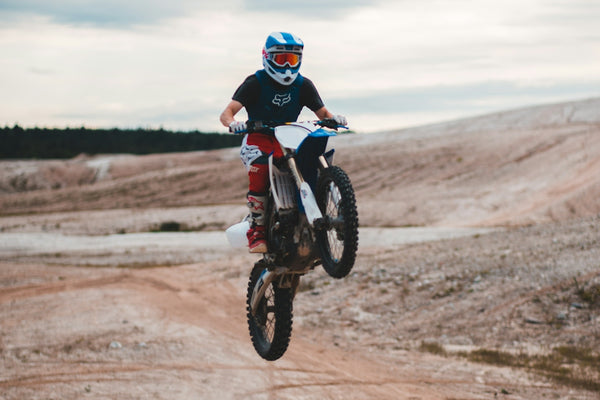 man in red and black motocross suit riding motocross dirt bike on brown dirt road during