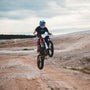 man in red and black motocross suit riding motocross dirt bike on brown dirt road during